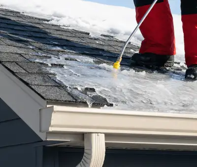 Ice dam removal technician using a steam wand to melt thick ice buildup on a residential roof in South Bend, IN