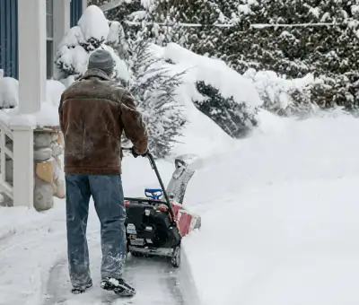 Residential snow removal technician using a snow blower to clear a home driveway and walkway in South Bend, IN