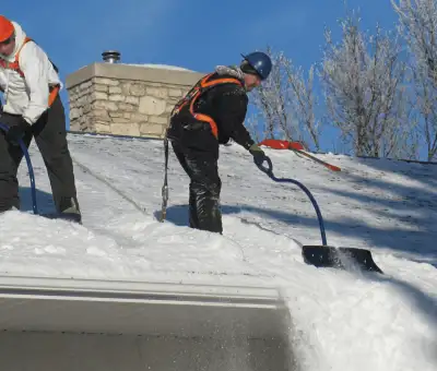Professional technicians performing roof snow removal with safety harnesses and shovels in South Bend, IN
